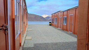Fileira de cabanes vermelles amb un camí de grava que condueix a un cos d'aigua i muntanyes al fons.