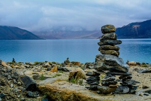 A stack of stones by a calm lake with mountains in the background. - Blue Chill Cottage Pangong (Leh)