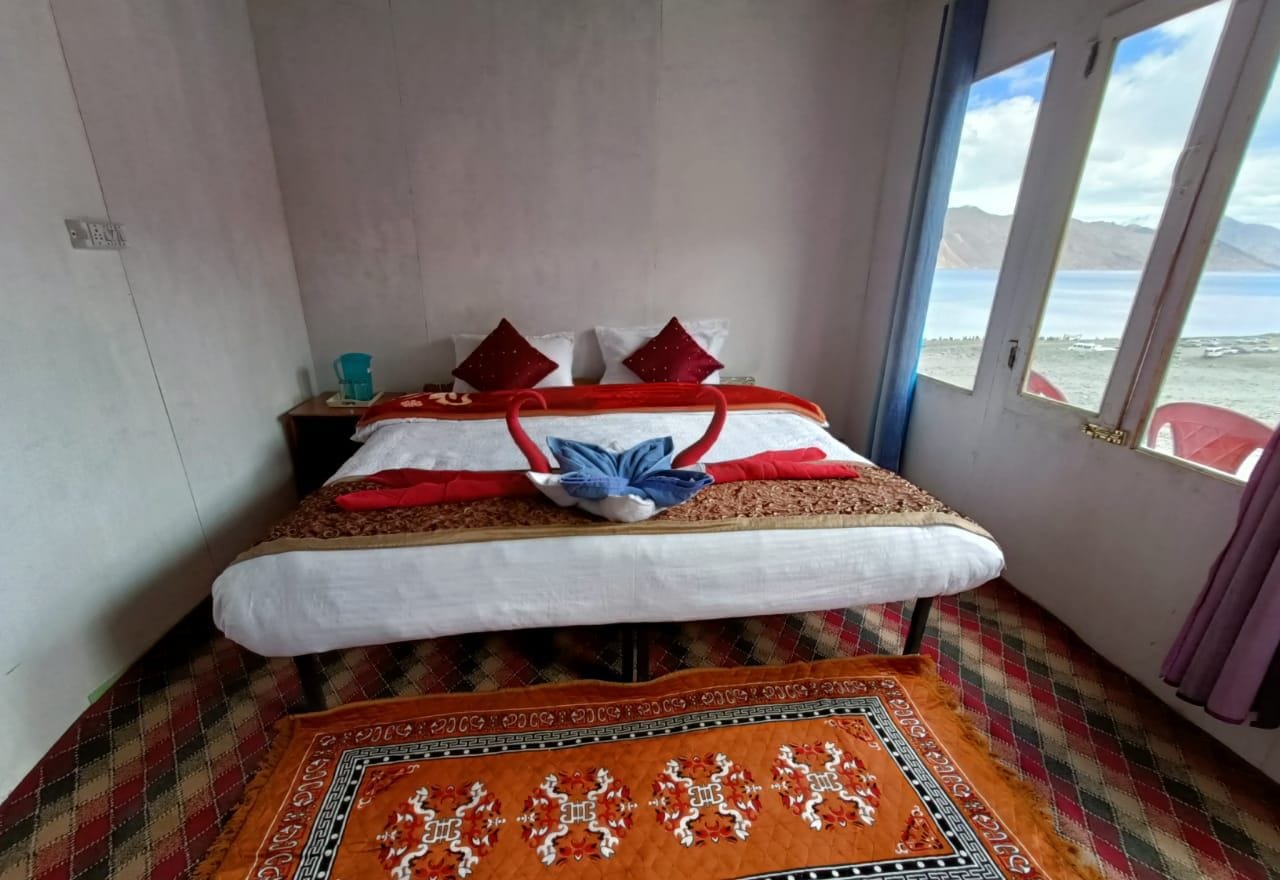 A bed with a red and white bedspread, a plaid rug, and a window with a view of the sea.