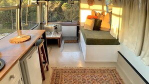 A compact RV interior with a kitchenette, a small dining table, a cushioned seating area, and a patterned rug. - The Bus Stop (Marion Bay)