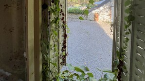 A window with overgrown ivy and a view of a gravel driveway leading to a stone building. - Maison & Pool in the Bourgogne (Saint-Nizier-sur-Arroux)