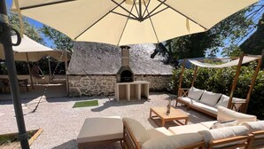 An outdoor patio with a stone fireplace, wooden furniture, and a large umbrella providing shade. - Maison & Pool in the Bourgogne (Saint-Nizier-sur-Arroux)