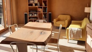 Una sala de estar moderna con una mesa de madera, dos sillas, un sofá amarillo y una estantería llena de libros y dispositivos electrónicos.