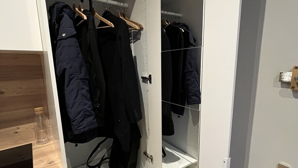A walk-in closet with hanging space and shelves, a wooden floor, and a white door with a brass handle. - La Madeleine Jolie Studio en Hyper Centre (Rennes)