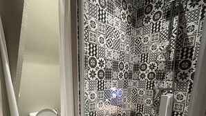 A bathroom with a patterned tile wall, a shower, and a toilet. - La Madeleine Jolie Studio en Hyper Centre (Rennes)