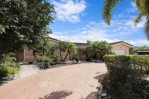 Um imóvel residencial com calçada pavimentada, palmeiras e um edifício com telhado de cerâmica.