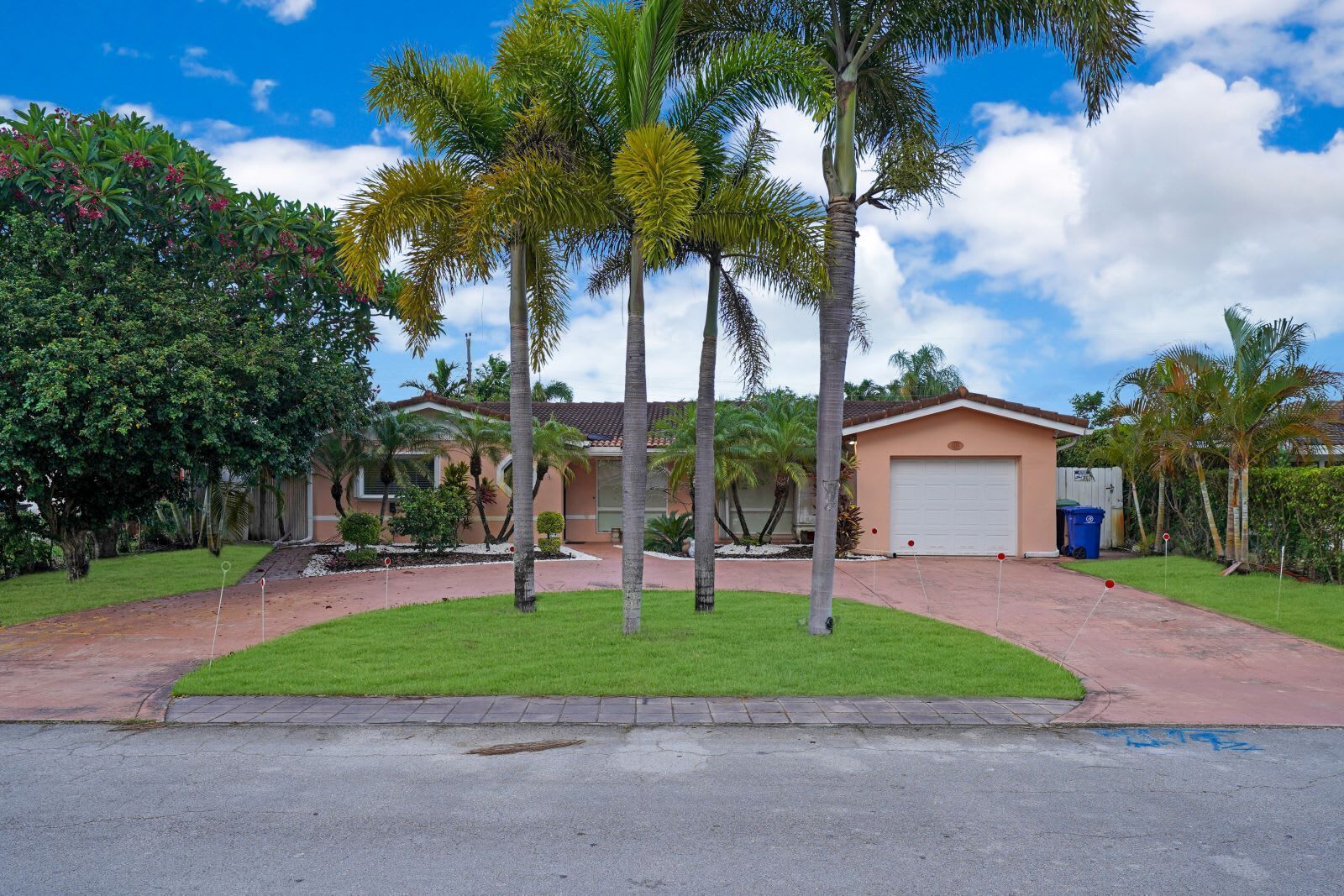 A residential property with a garage, a well-maintained lawn, and palm trees.