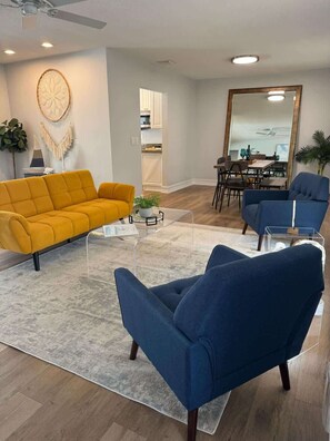 Uma sala de estar moderna com sofá, poltronas, mesa de centro e um espaço de jantar com espelho.