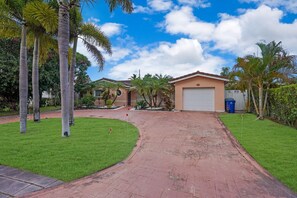 A residential property with a paved driveway, palm trees, and a garage.
