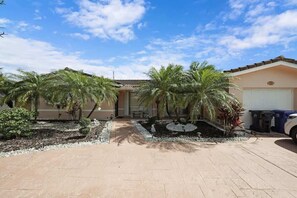Um imóvel residencial com entrada por meio de um caminho de acesso, palmeiras e garagem.
