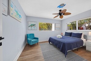 Ein Schlafzimmer mit einem Bett, einem Sessel, einem Deckenventilator und Bildern an der Wand.