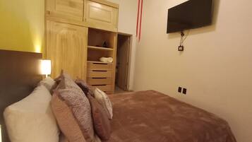 Ein Schlafzimmer mit Bett, Kleiderschrank, Wandfernseher und Nachttischlampe.