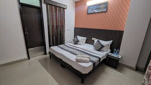 Un dormitorio ordenado con cama, almohadas, una mesita de noche con botellas de agua y un cuadro en la pared.