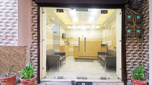 Zona de recepción con puerta de vidrio, mostrador de recepción, dos sofás y plantas en macetas.