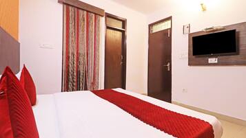 Une chambre d’hôtel avec un lit, des oreillers rouges, un téléviseur fixé au mur et une porte ornée d’un rideau à rayures.