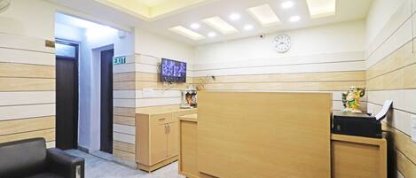 A reception area with a wooden reception desk, two black chairs, a clock, and a television mounted on the wall.