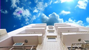 Vista de un edificio con varias estructuras blancas y un cielo azul despejado con nubes.