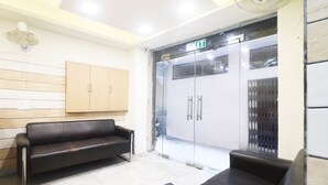 Un área de recepción con un sofá de cuero negro, un mueble de madera y una puerta de cristal con una señal de salida.