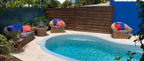 Un patio trasero con piscina, muebles de mimbre y plantas en macetas.