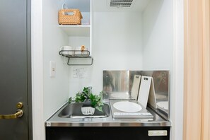 Un espace cuisine compact comprenant un évier, une petite étagère avec un panier et un appareil fixé au mur.