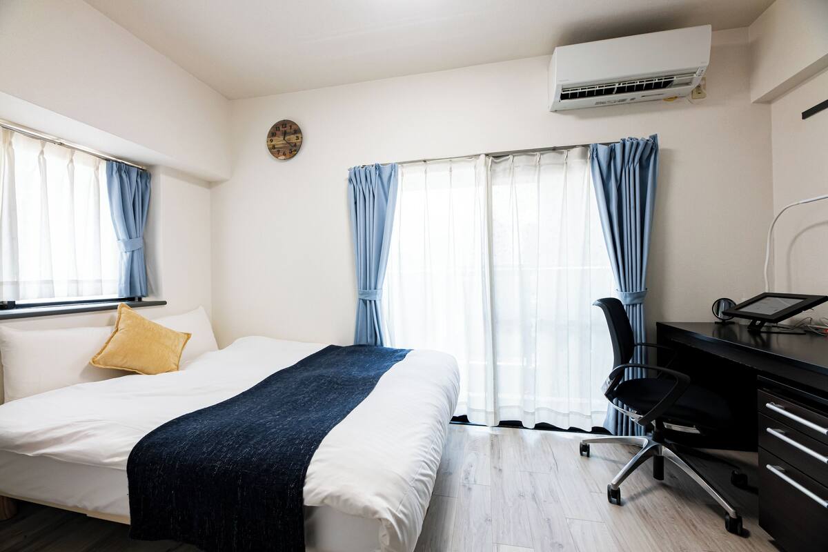 A bedroom with a bed, a desk, and an air conditioner.