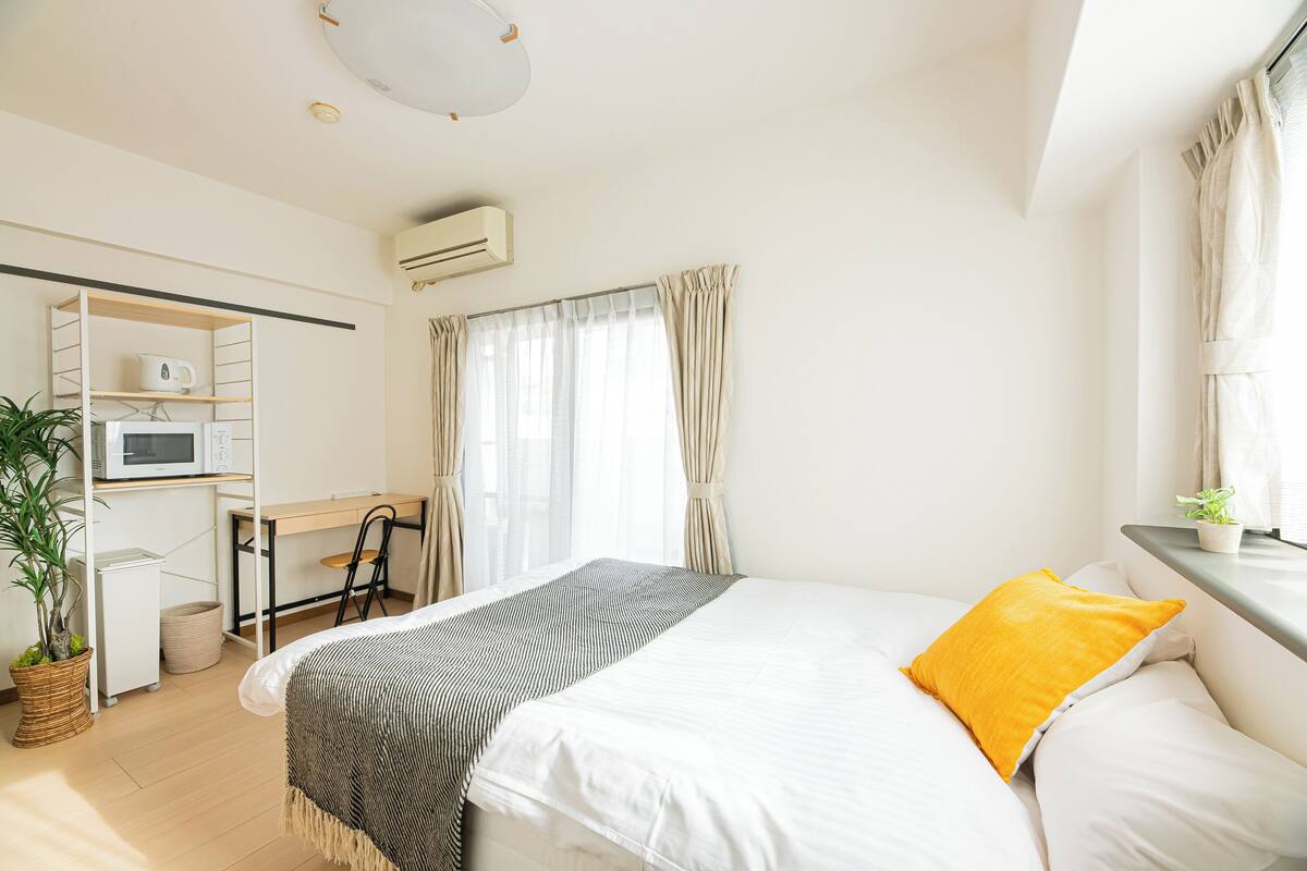 A neatly arranged bedroom with a bed, bedside table, and a desk area with a chair.