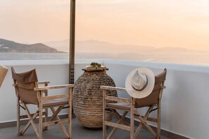 Two wooden chairs with cushions, a large textured vase, and a straw hat on a balcony overlooking a body of water and distant mountains. - Kastro Suite in Naxos Old Town (Naxos)