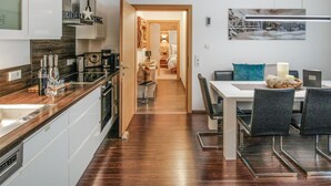 Une cuisine moderne dotée d’un plan de travail en bois, d’appareils électroménagers en acier inoxydable et offrant une vue sur l’espace repas, avec une table et des chaises.