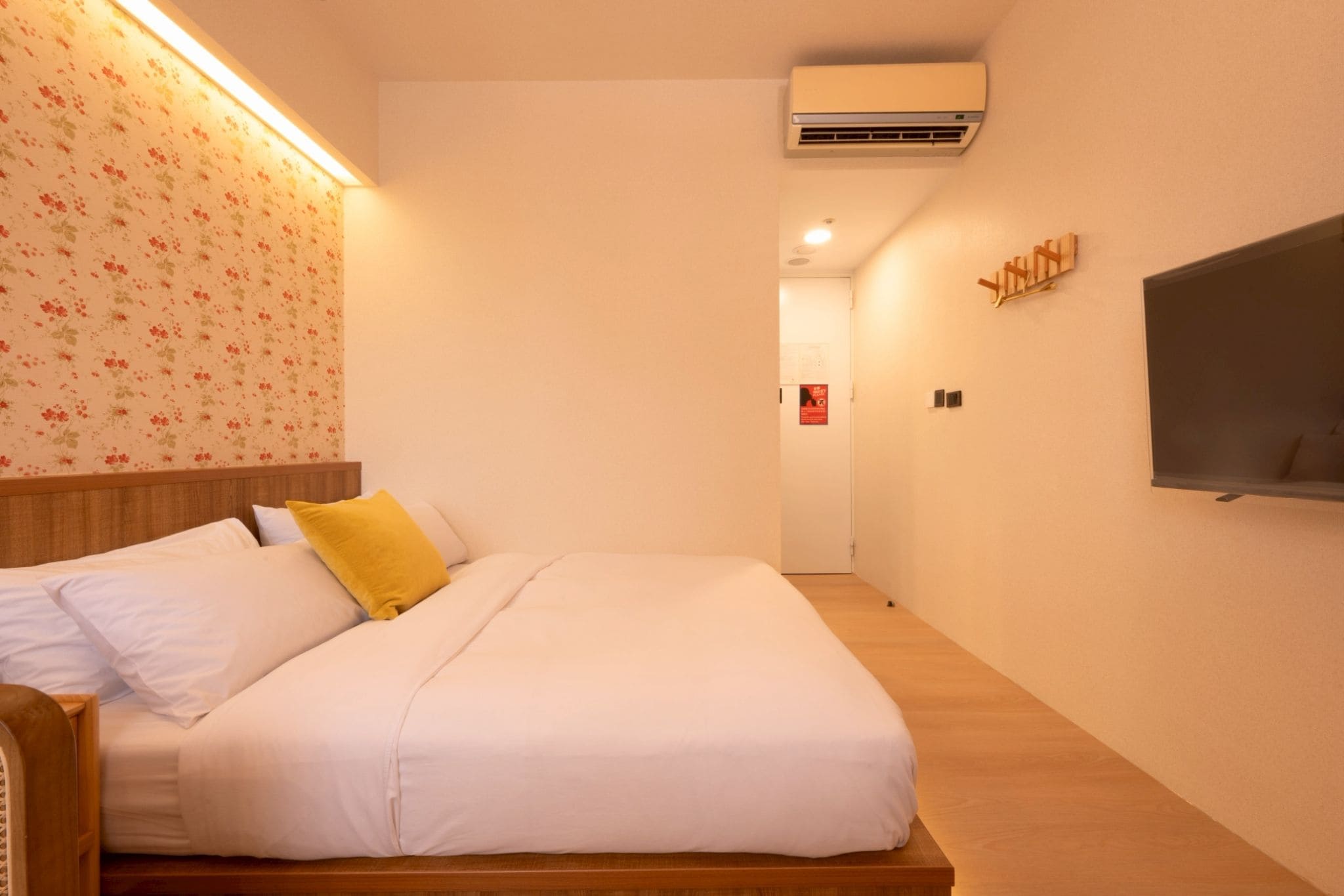 A hotel room with a bed, a wall-mounted TV, an air conditioning unit, and a wooden floor.