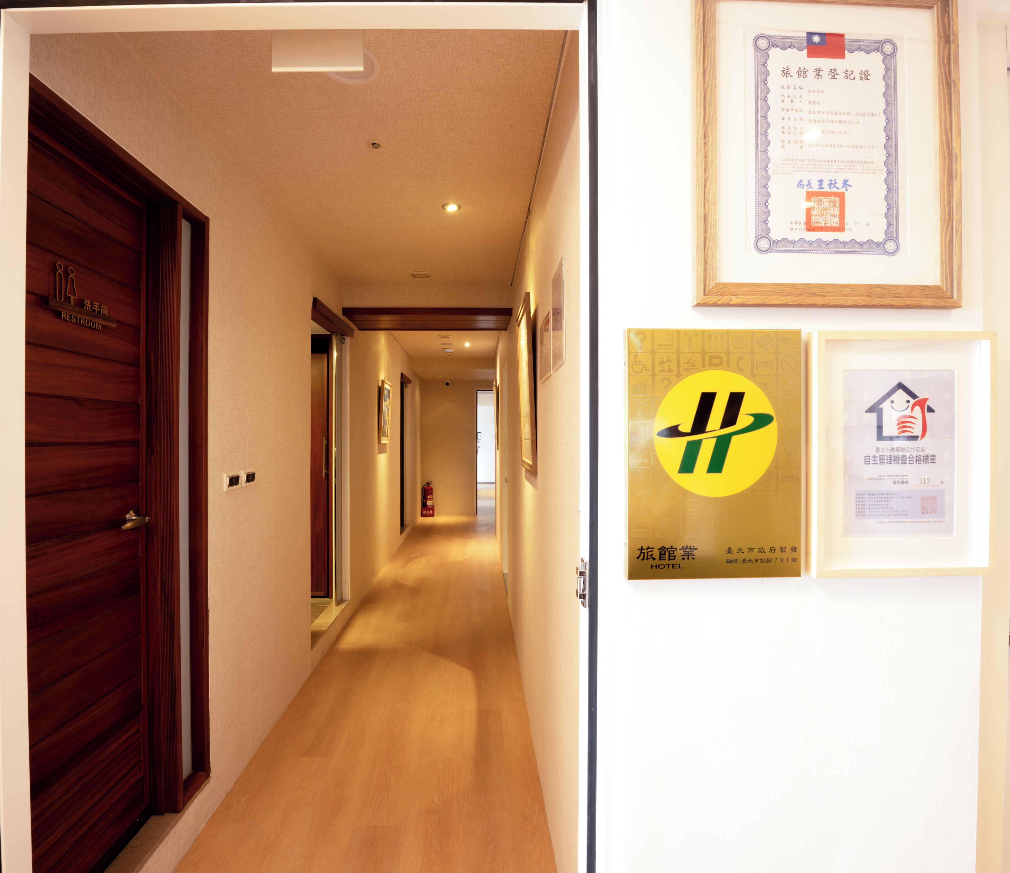 Een hotelgangen met houten deuren, een brandblusser en ingelijste certificaten aan de muur.