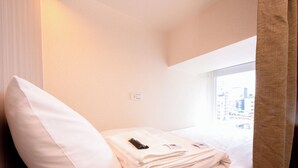 A hotel room with a bed, a window with a city view, a bedside table with a remote control, and a power outlet on the wall. - Cattail pocket Inn (Taipei)