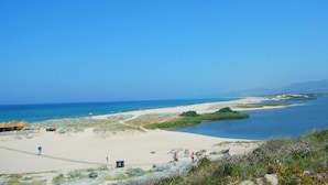 A coastal landscape with a sandy beach, a clear blue sky, and a few people walking.