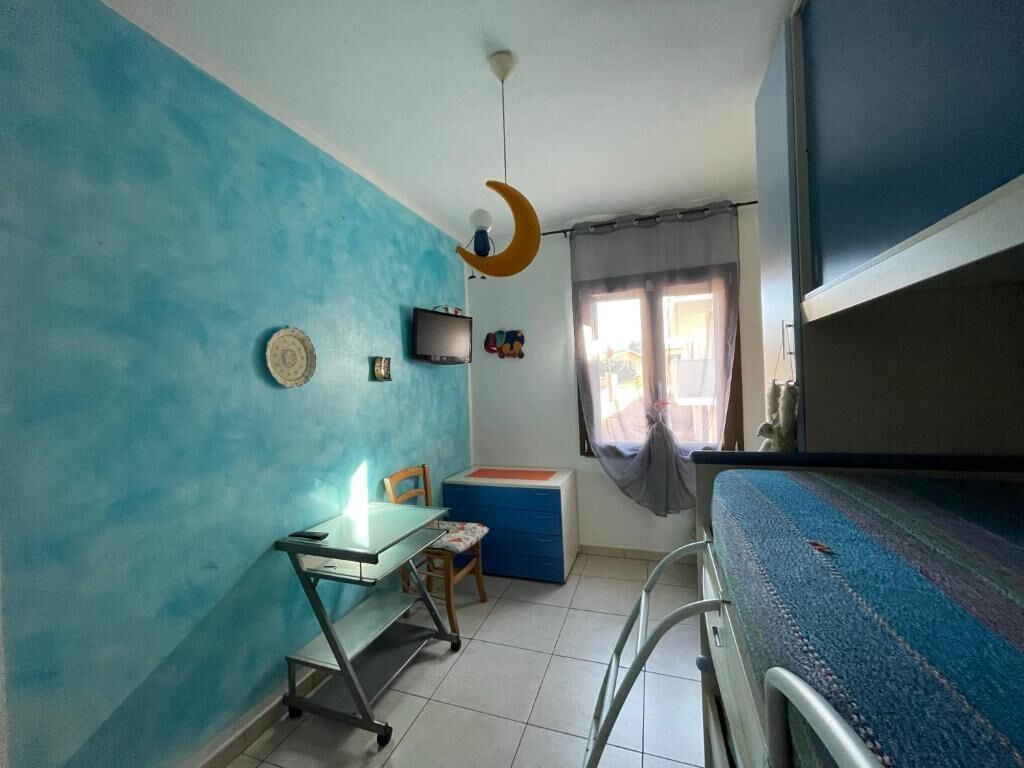 Une chambre avec un lit superposé, un bureau avec une chaise, une petite table, un téléviseur et une fenêtre avec des rideaux.