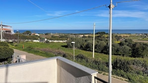 A coastal view from a balcony with a clear sky, a road, and distant buildings.