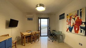 A room with a dining table, chairs, a TV, a desk with a chair, and a large abstract painting.