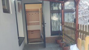 Ein überdachter Außenbereich mit einer Holztür, Kübelpflanzen und einem Holzzaun.