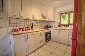 A kitchen with white cabinets, a tiled backsplash, and a window with a view of greenery.