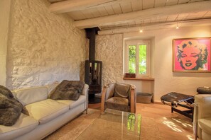 A cozy living room with a stone wall, a fireplace, a sofa, a chair, and a painting.