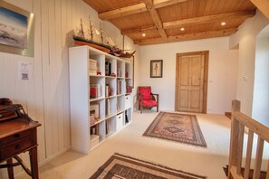 A room with a wooden ceiling, a bookshelf, a red chair, and a patterned rug.