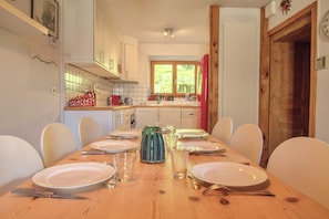 A dining table set with plates, cutlery, and glasses in a room with a window, wooden door, and white walls.
