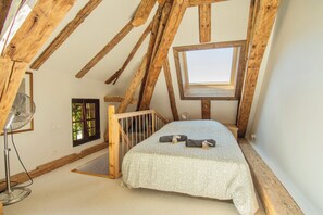 A small, attic-style bedroom with a sloped ceiling, a single bed with a patterned bedspread, a standing fan, and a skylight.