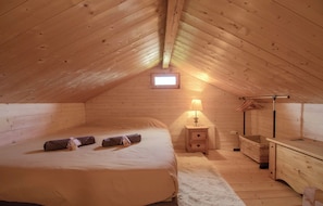 A cozy attic bedroom with a bed, bedside table, lamp, and a small window.
