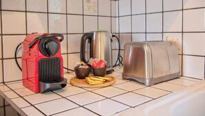 Un plan de travail de cuisine avec une cafetière rouge, une bouilloire argentée, un grille-pain et un panier contenant du pain et une tasse.