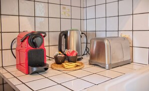 A kitchen counter with a red coffee maker, a silver kettle, a toaster, and a basket with bread and a cup.
