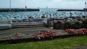 Un port de plaisance où sont amarrés de nombreux bateaux, un mât avec un drapeau, et une vue sur la mer.
