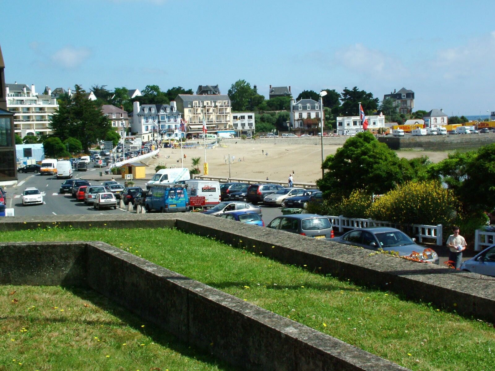 A coastal town with a sandy beach, parked cars, and buildings in the background.
