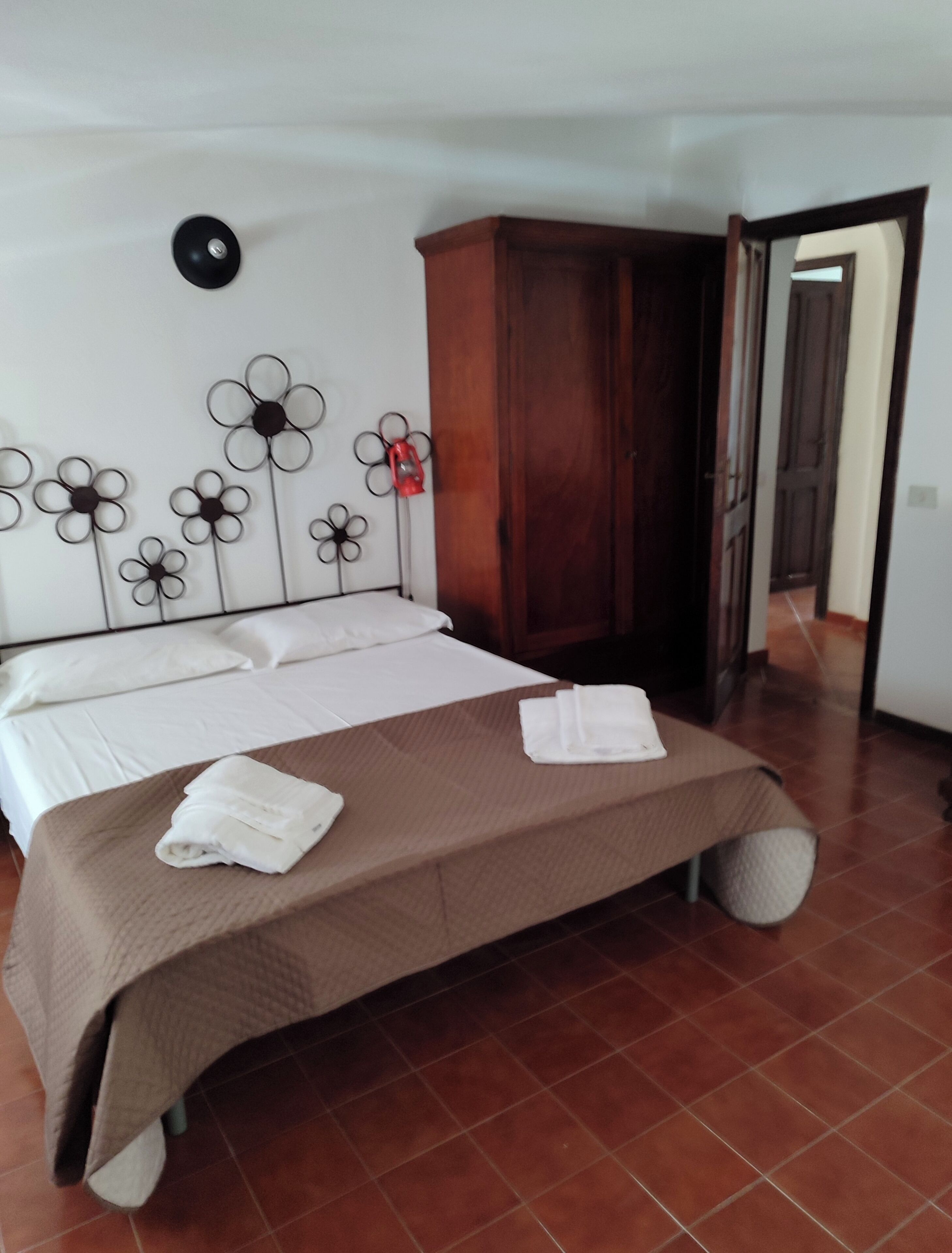 A hotel room with a bed, a wooden wardrobe, and a wall decoration of flowers.