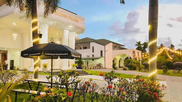 Ein Hotel namens 'Hotel Royal Grand Paradise' mit einem gepflegten Garten, Sitzgelegenheiten im Freien und freiem Blick auf den Haupteingang des Gebäudes.