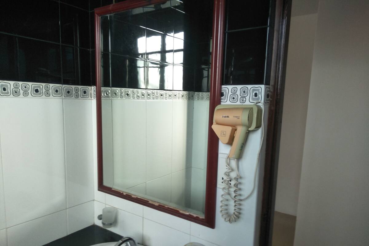 Ein Badezimmer mit einem weißen Waschbecken, einem Spiegel mit rotem Rahmen und einem an der Wand montierten Fön.