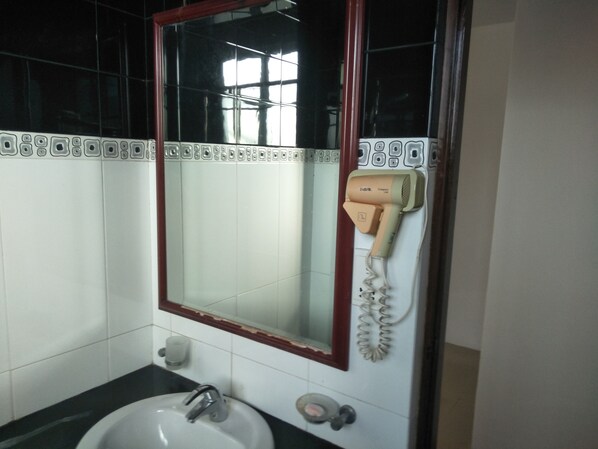 A bathroom with a white sink, a mirror with a red frame, and a hairdryer mounted on the wall. - Airport Hotel Dream Paradise (Seeduwa - Katunayake)
